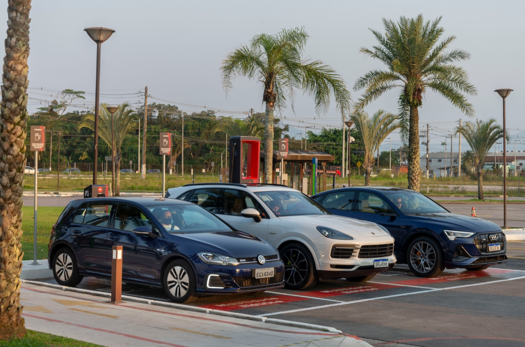 Veículos estacionados em eletroposto com equipamentos de recarga ao fundo